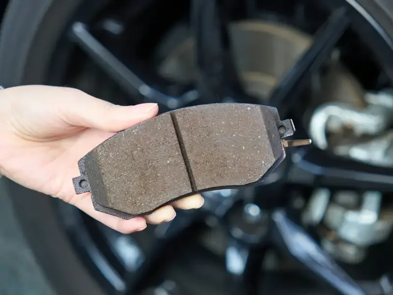 Hand holding a brake pad in front of a wheel